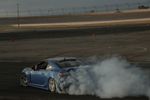 Free A blue car drifts with smoke trailing on a race track, showcasing speed and skill. Stock Photo