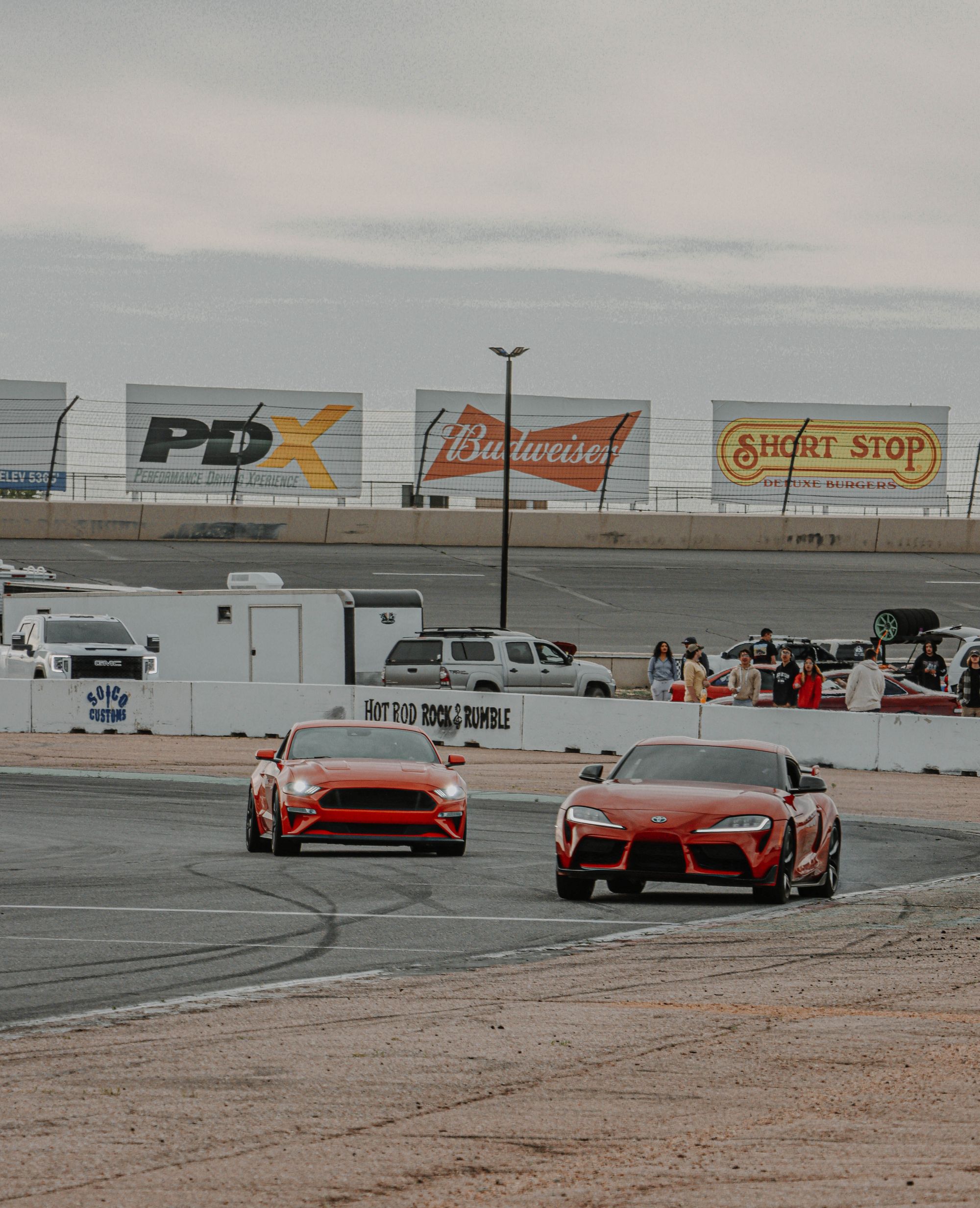Shows a Ford Mustang and Toyota Supra racing side-by-side on a track, directly illustrating the rival comparison theme.