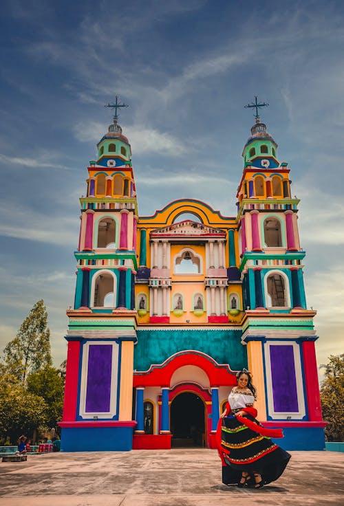 Woman in Traditional Dress Dancing near Colorful Church 