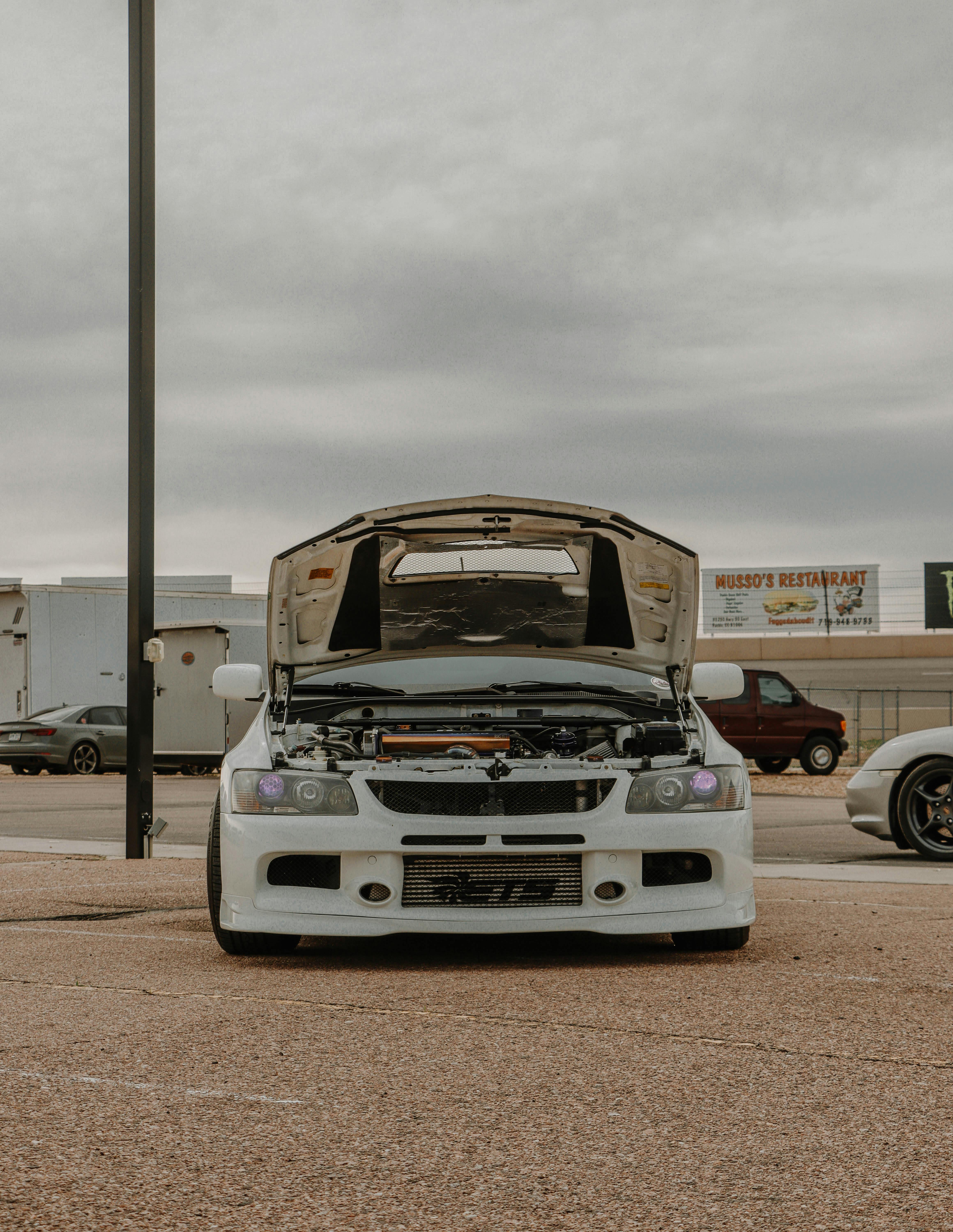 A white Mitsubishi car parked with its hood open, captured in an outdoor setting.