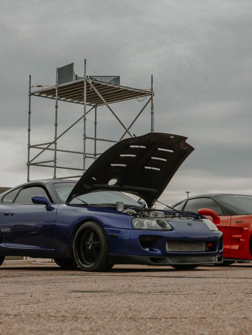 Free Two Toyota Supra cars showcased at an outdoor car event with open hood and scaffolding backdrop. Stock Photo