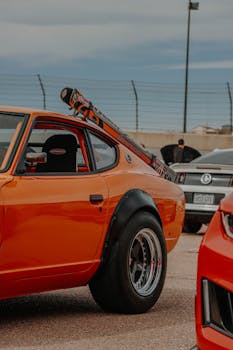 Orange Datsun sports car with modifications visible at an outdoor automotive show for enthusiasts.