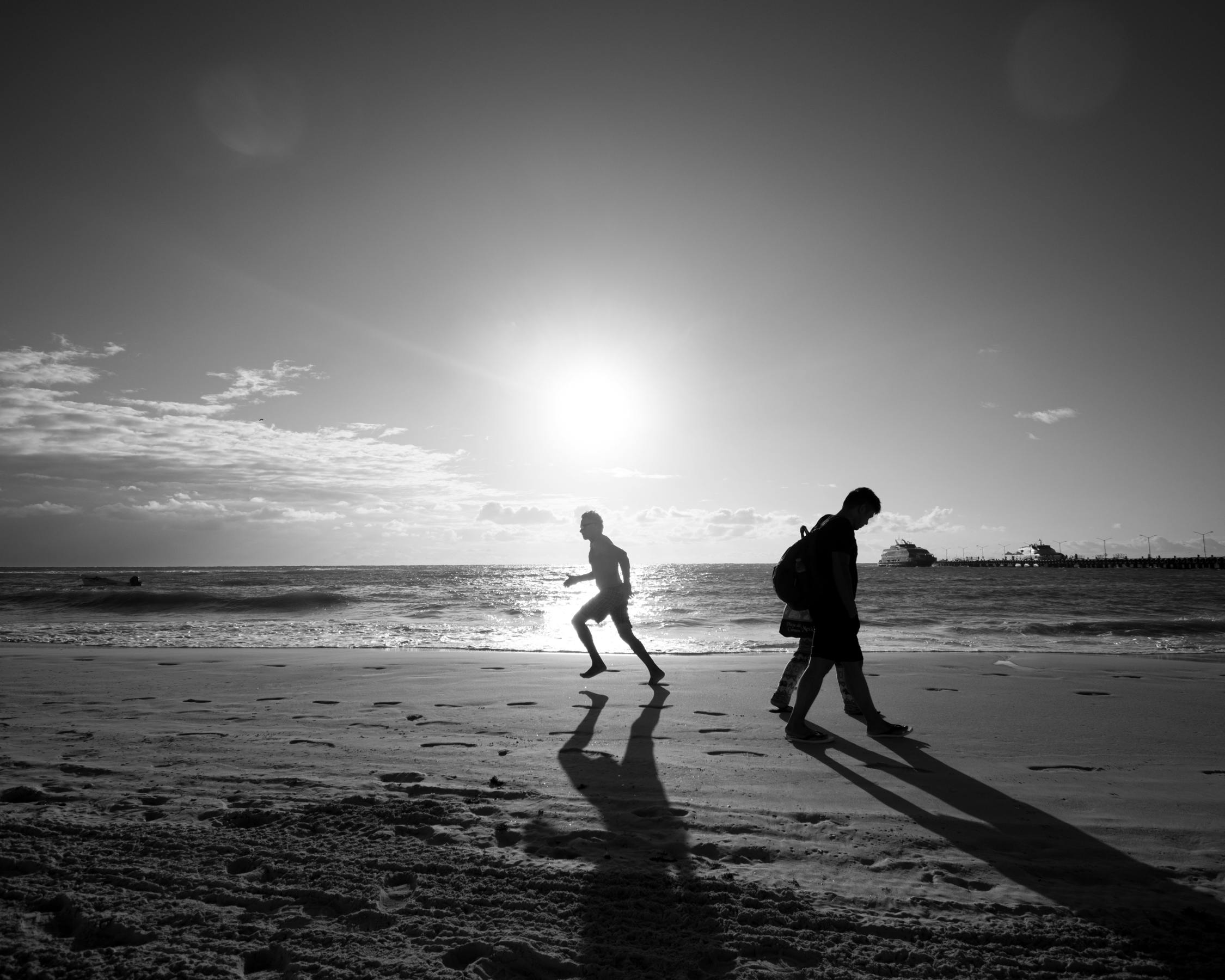 Silhouettes of people walking on the Cancún beach at sunset, capturing serene coastal beauty.