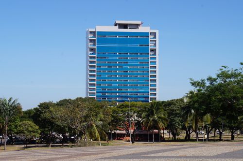 Free A striking modern blue building facade amidst green trees under a clear sky. Stock Photo