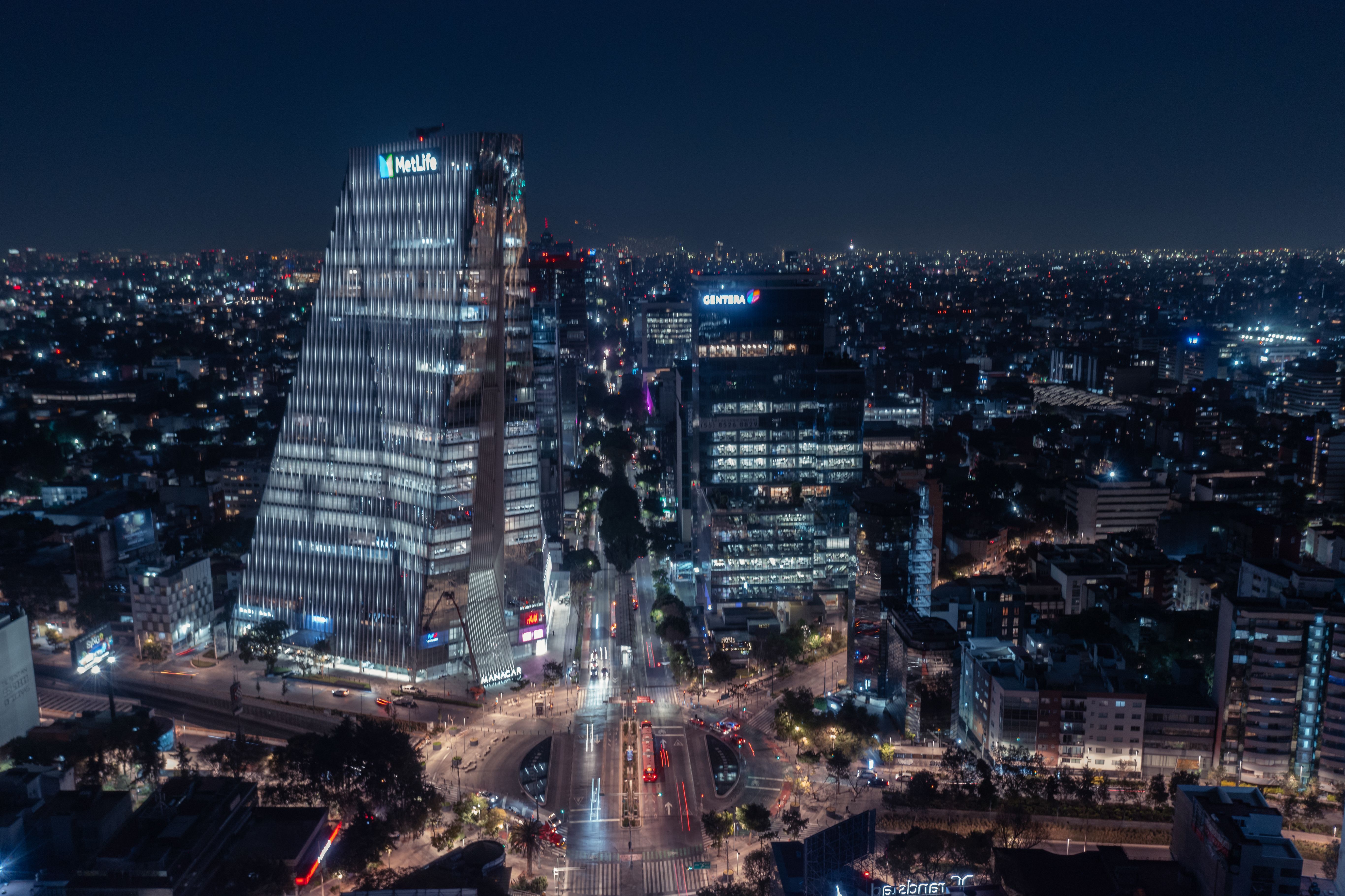 A stunning aerial view of a bustling city skyline at night, featuring illuminated skyscrapers and a busy roundabout.