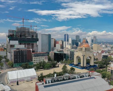 An aerial shot of Mexico City showcasing skyscrapers and the Monument to the Revolution under a blue sky.