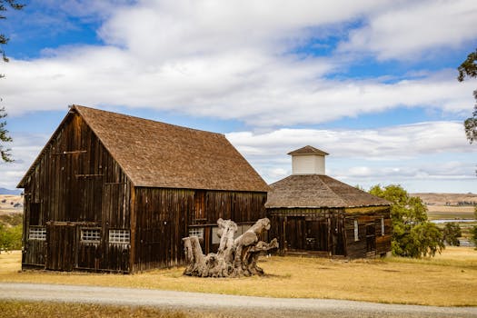 A scenic view of a rustic wooden barn in a rural countryside setting under a blue sky.