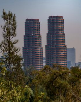 An urban skyline featuring modern twin towers amidst green foliage and city buildings.