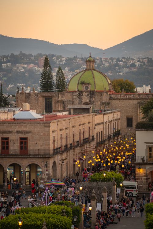 Free A vibrant street scene in a historic Mexican town at dusk, bustling with people and lights. Stock Photo