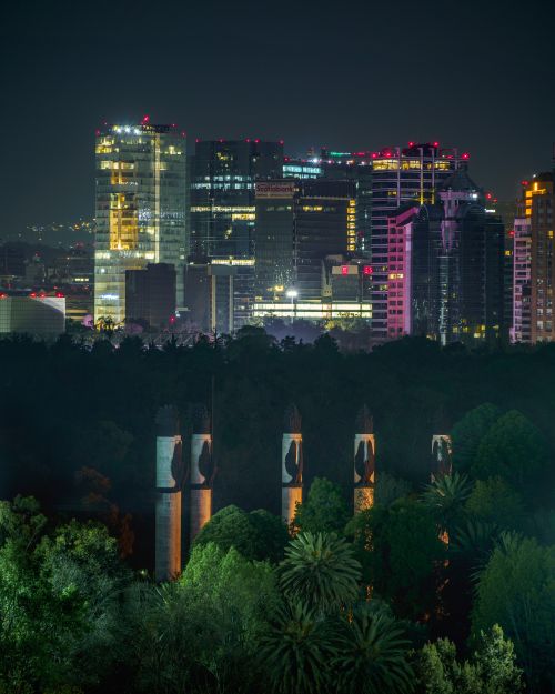 Free Stunning Mexico City skyline at night featuring illuminated buildings and lush greenery foreground. Stock Photo