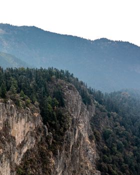 A breathtaking view of a lush forest atop a rugged mountain cliff under a clear sky.