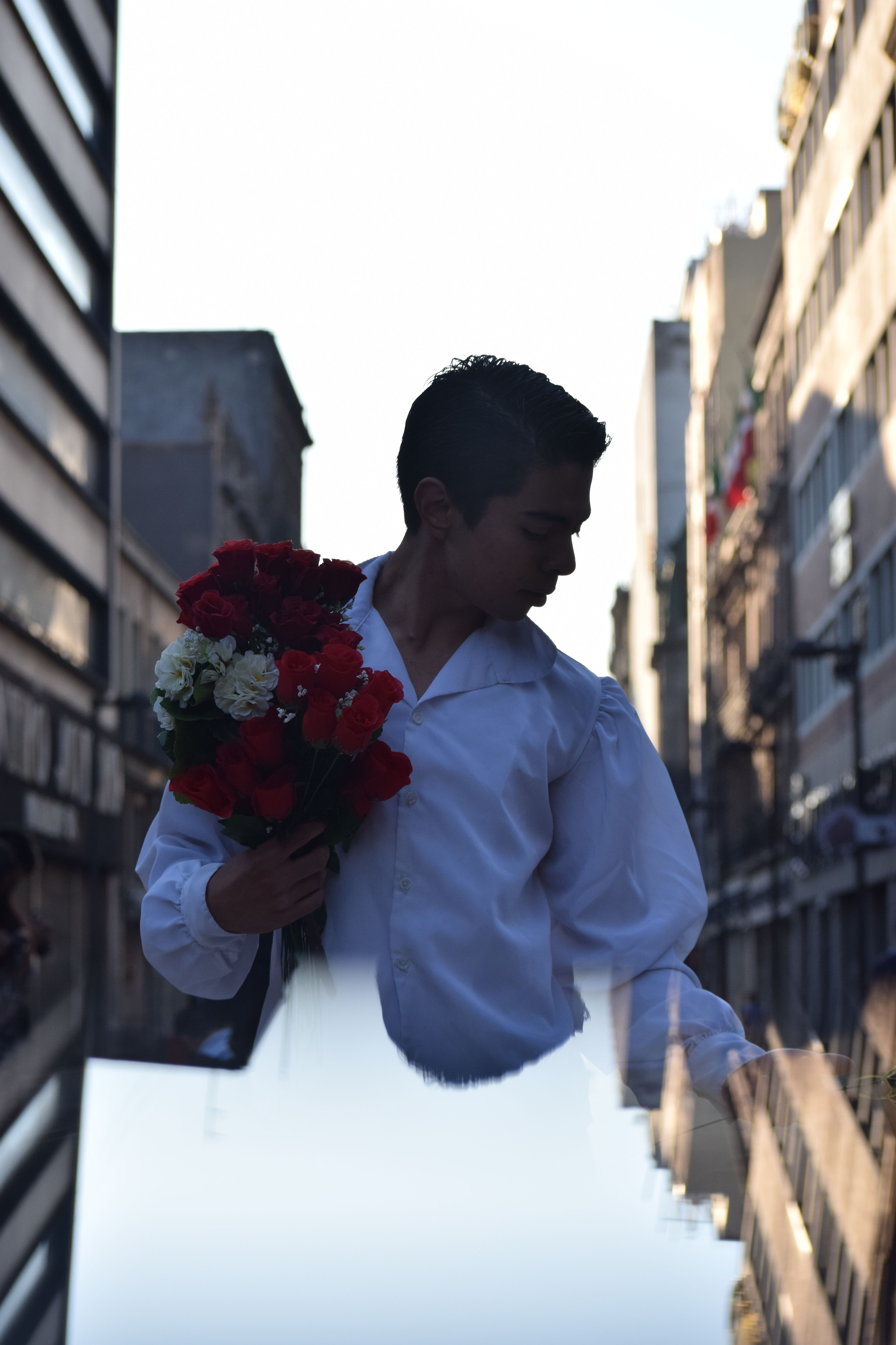 A young man holds a bouquet of red and white flowers on a bustling city street, captured at sunset.