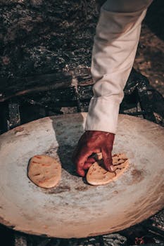 Hand placing flatbread on a traditional open flame griddle showcasing cultural culinary methods.