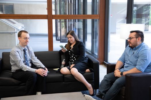 Three colleagues having a casual discussion in a modern office lounge area, focusing on teamwork and collaboration.