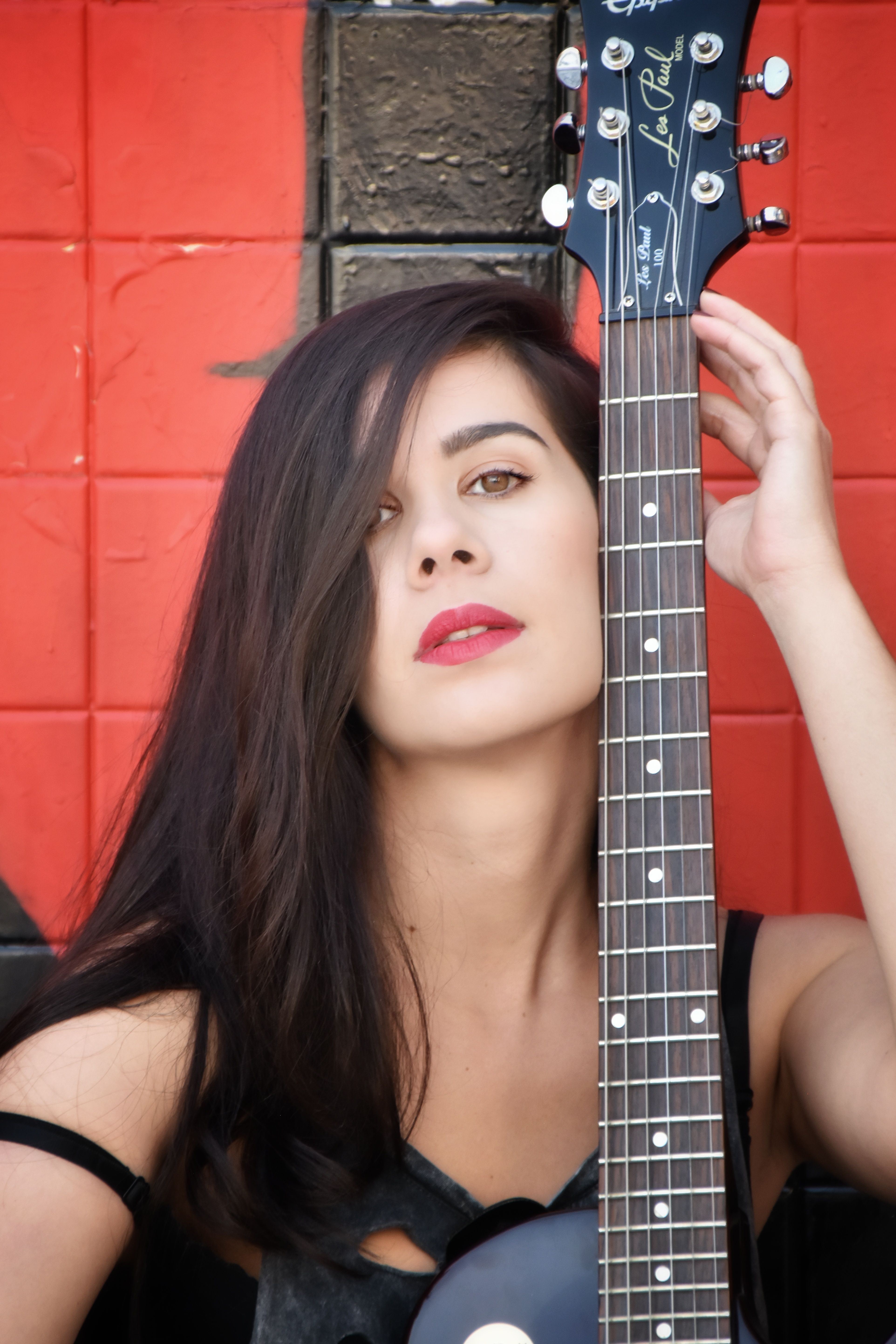 Stylish woman holding a guitar against a red backdrop, exuding modern artistry.