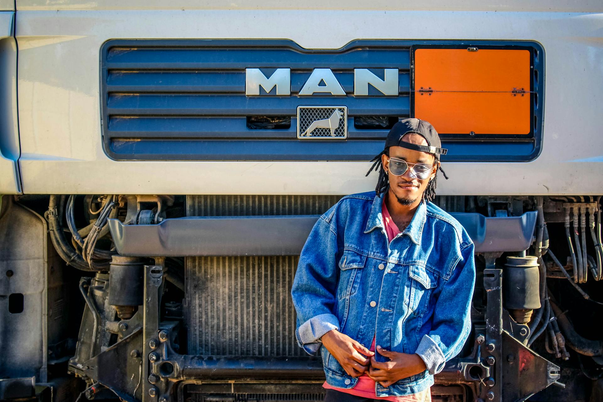 Confident young man in denim jacket poses in front of a MAN truck outdoors.