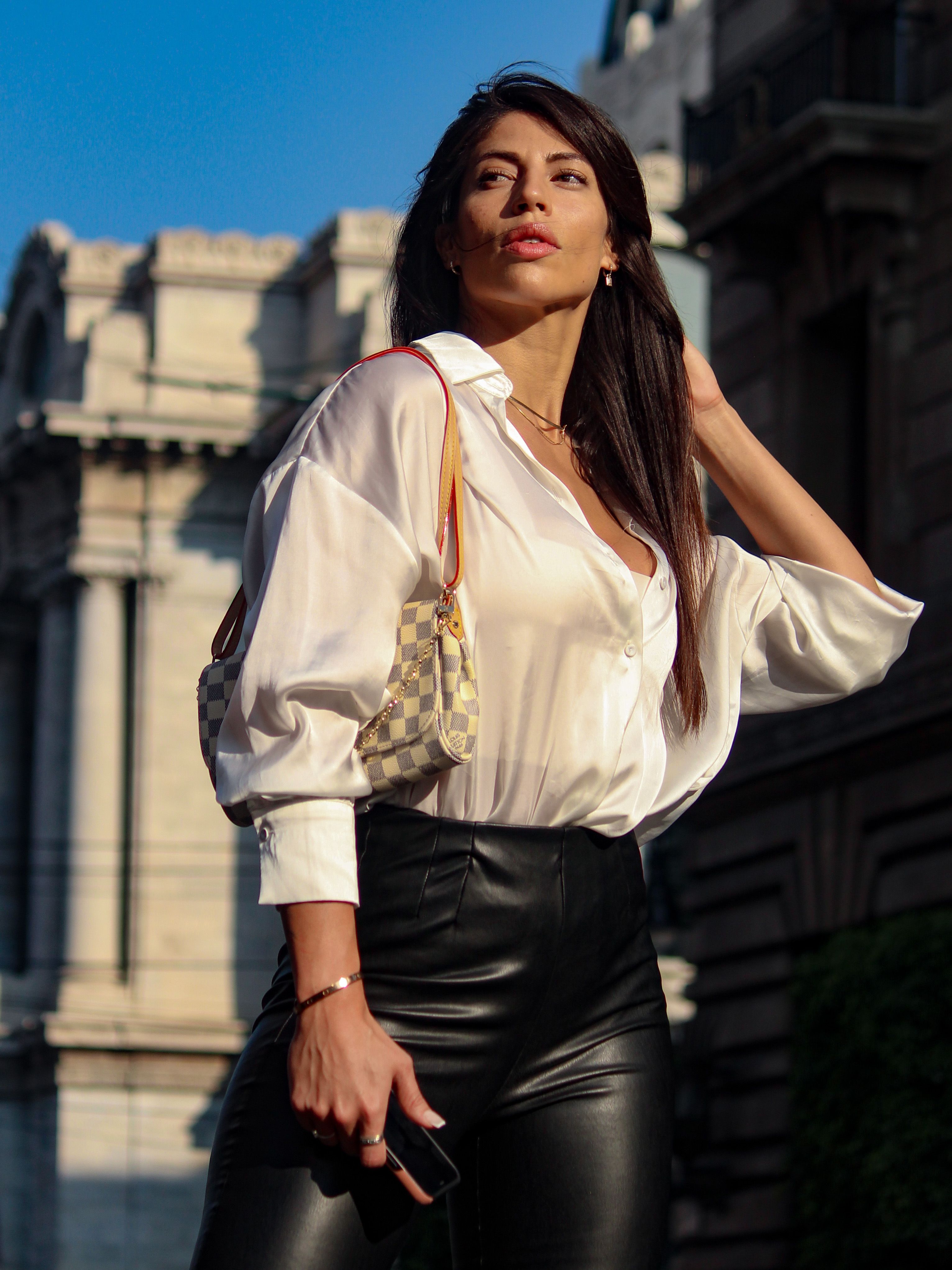 Mulher estilosa em calças de couro e blusa branca, posando com confiança na Cidade do México.