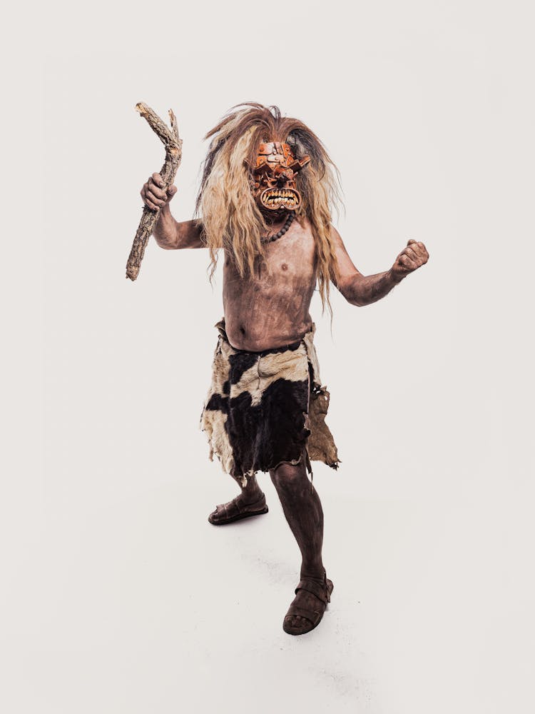 Studio Shot Of A Man In A Leather Carnival Costume And Mask Holding A Stick