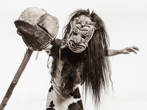 Sepia Toned Studio Shot of a Man in a Fur Carnival Costume and Mask with a Stick