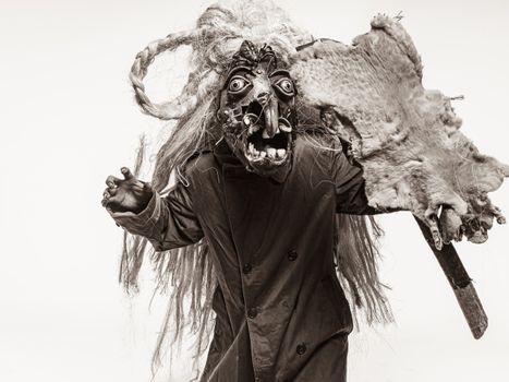 Sepia image of a person in a traditional Mexican carnival costume with mask, fur, and stick.