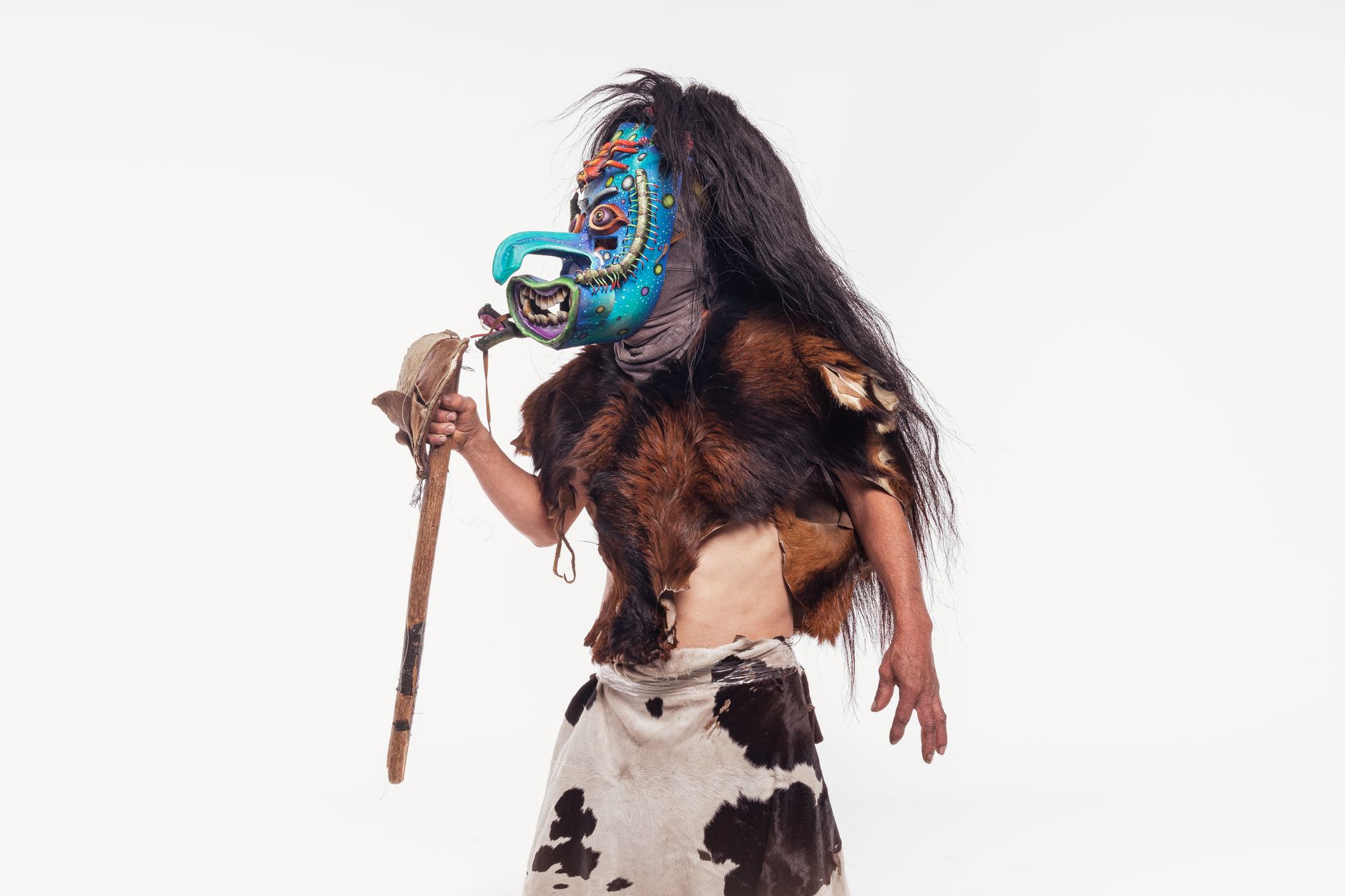 A person in traditional Mexican attire with a colorful mask standing against a white background.