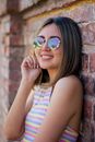Portrait of a Young Woman in Sunglasses Leaning on a Brick Wall 