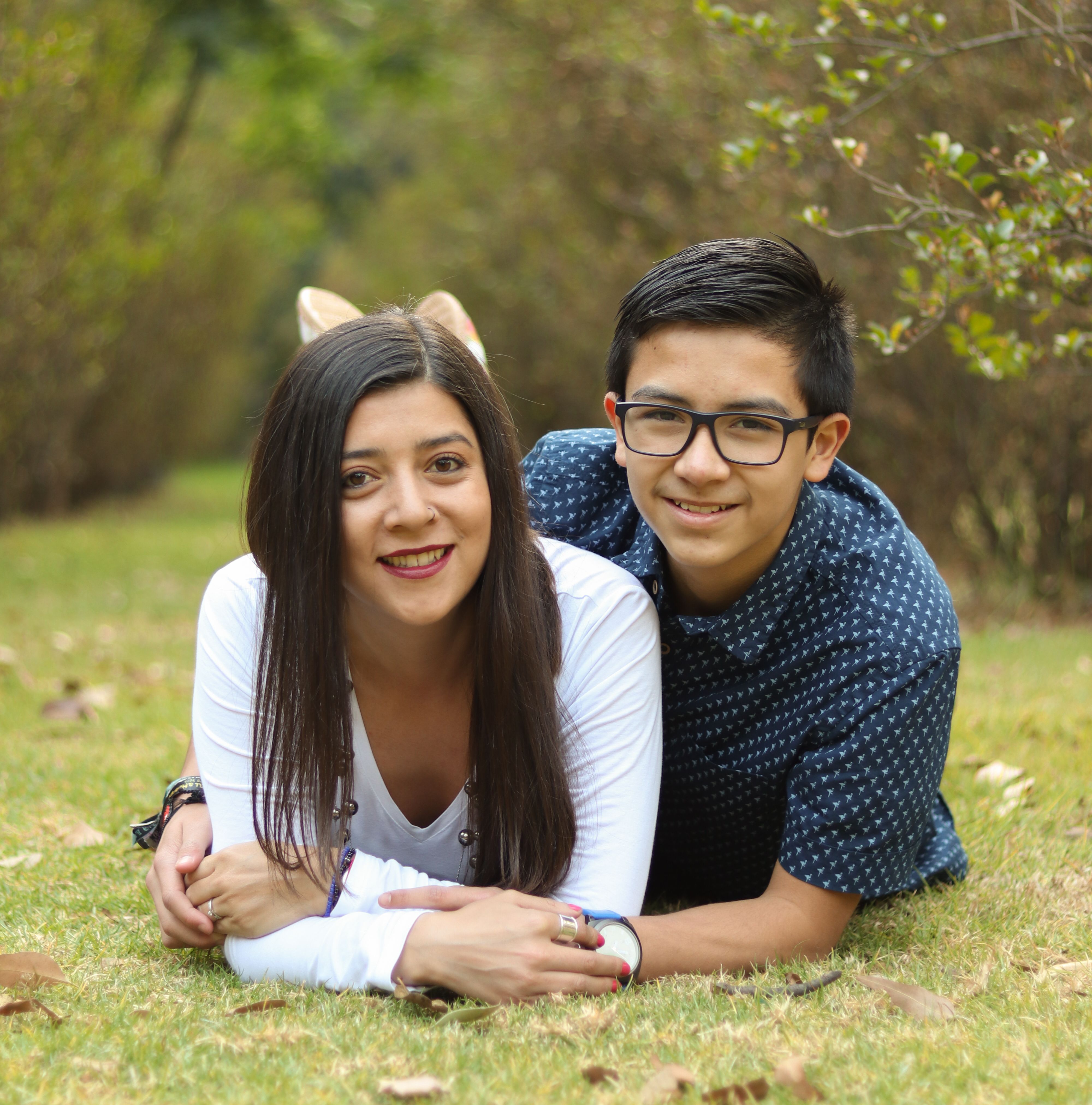 A brother and sister lying on the grass and smiling in a park, showcasing family love.