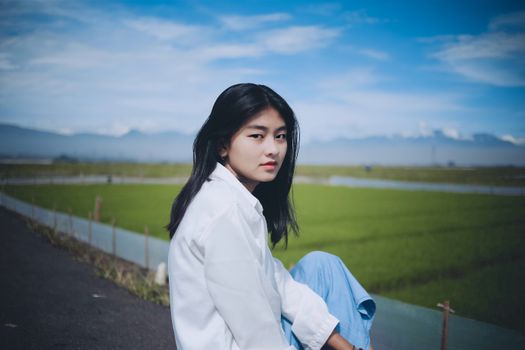 Portrait of a woman in Indonesia posing by a vibrant green rice field under a blue sky.