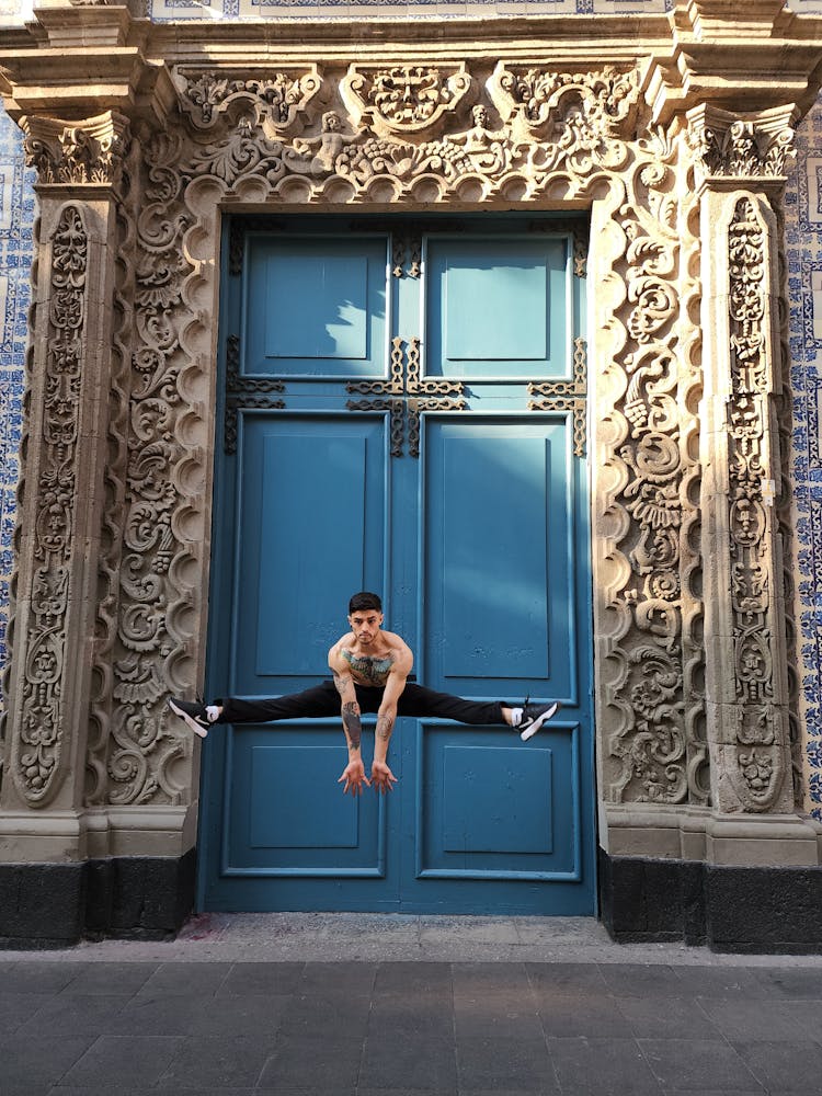 A Man Doing A Jump Split In Front Of Double Doors