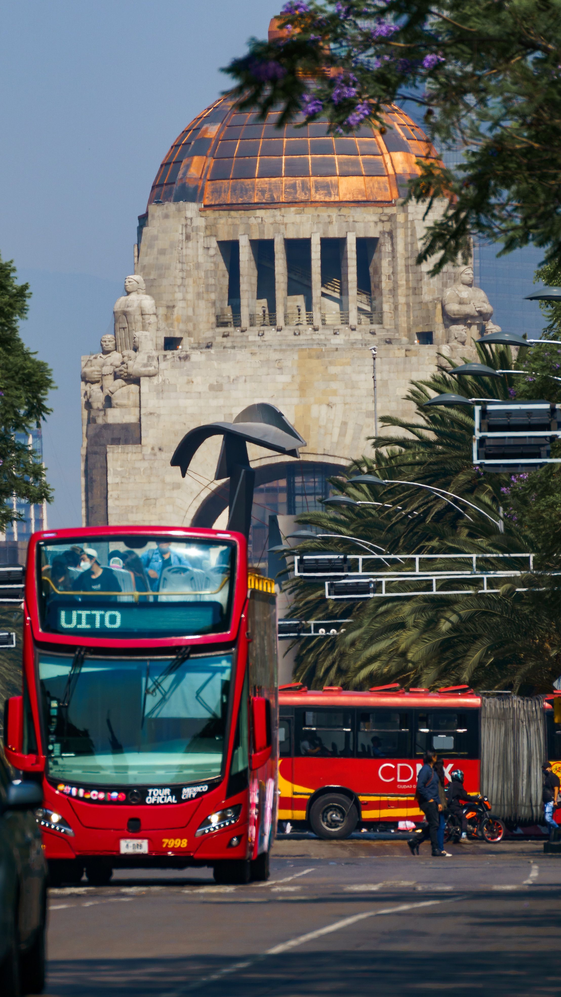 Urban traffic in Mexico City with buses and cars near a landmark monument