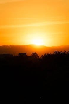 A vibrant sunset casting an orange glow over a silhouetted landscape, creating a serene atmosphere.