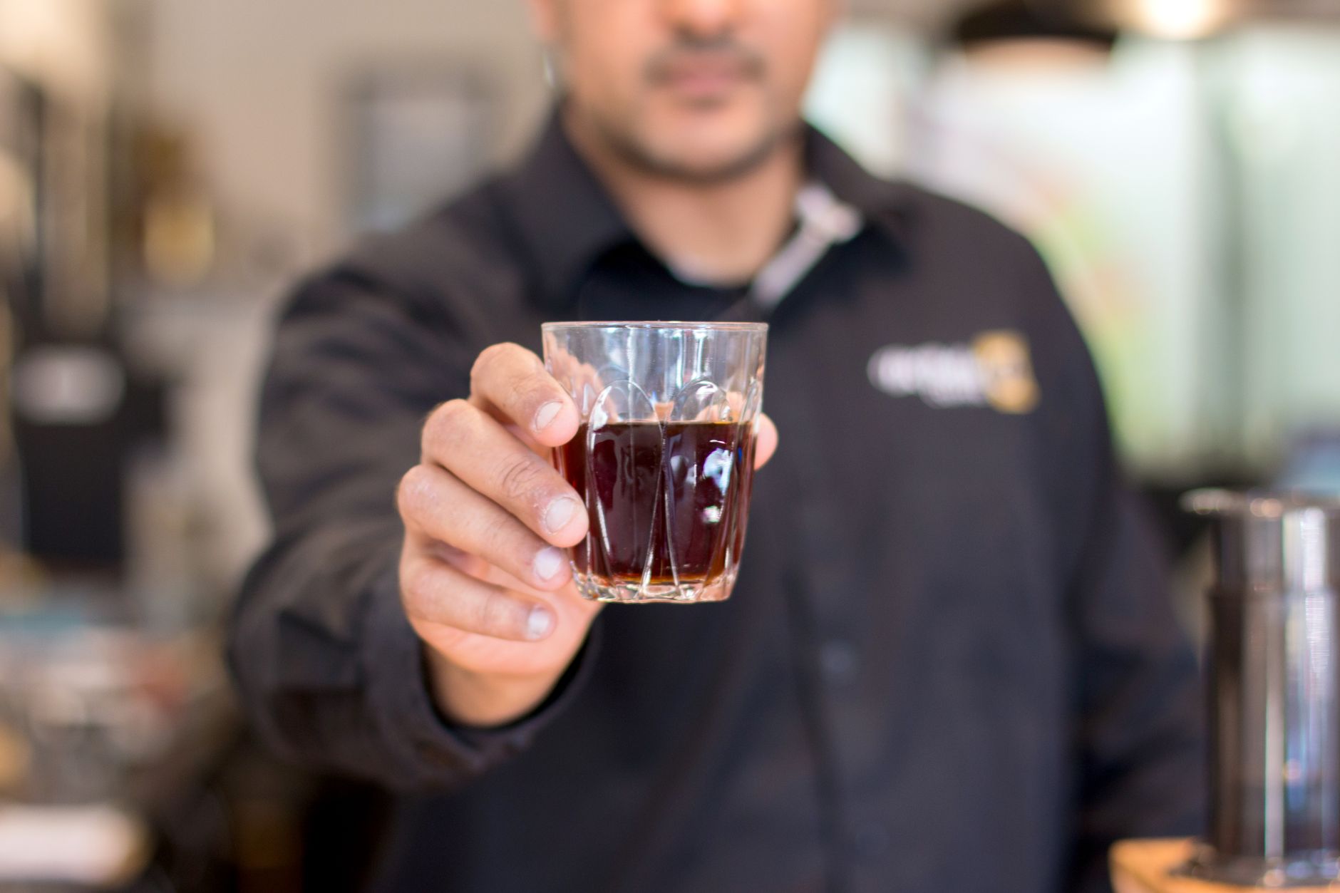 Barista presenting a glass of brewed coffee in a cozy café setting, perfect for lifestyle and beverage themes.
