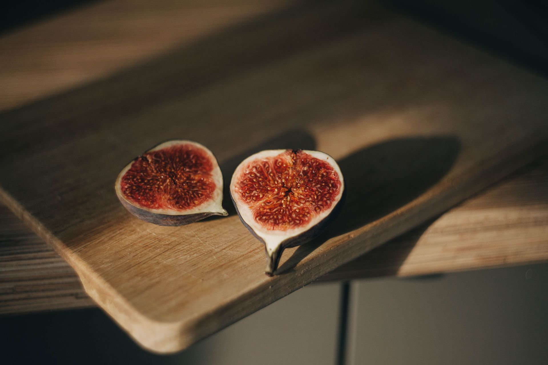 A close-up of halved figs on a wooden cutting board with soft, natural lighting creating an earthy still life scene.