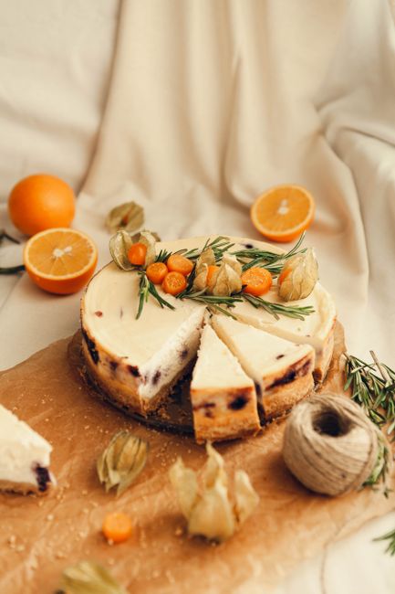 Cheesecake with citrus fruits and rosemary on rustic parchment paper, perfect for gourmet presentations.