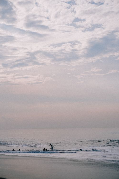Free A tranquil beach scene at sunset with silhouettes of people swimming in the ocean. Stock Photo