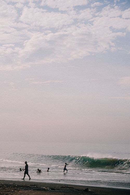 Free A peaceful beach scene with people swimming and enjoying the waves under a cloudy sky. Stock Photo