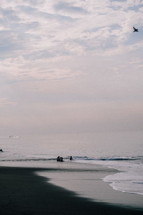 Free A tranquil beach scene at dusk with silhouettes of people and a dramatic sky, perfect for serene and peaceful imagery. Stock Photo