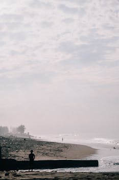 A serene seacoast view featuring a moody sky and silhouetted figures on the beach.