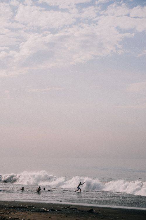 Free A tranquil scene of people enjoying the beach and waves under a cloudy sky. Stock Photo