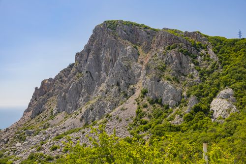 Free Breathtaking view of a rocky mountainside surrounded by lush greenery under a clear blue sky. Stock Photo