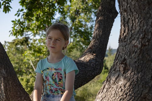 Free A Girl in Green Shirt Sitting on Brown Tree Trunk Stock Photo