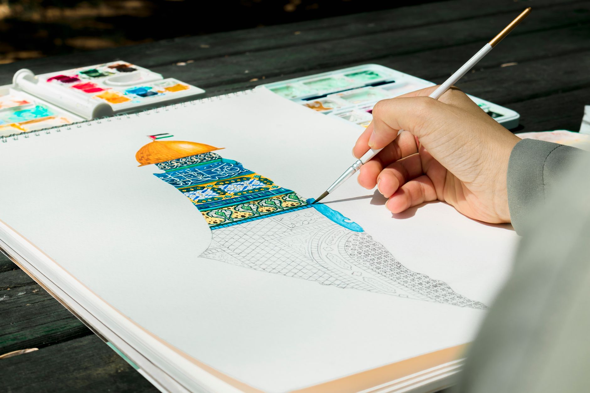 Close-up of a hand painting the Dome of the Rock in watercolor outdoors.