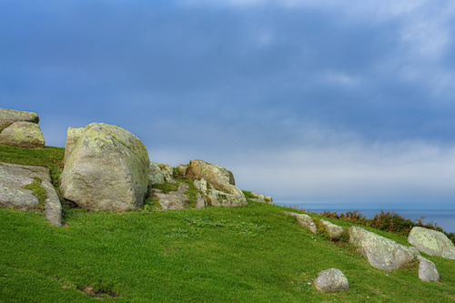 Free Tranquil coastal landscape featuring large boulders, lush grass, and a vibrant blue sky. Stock Photo