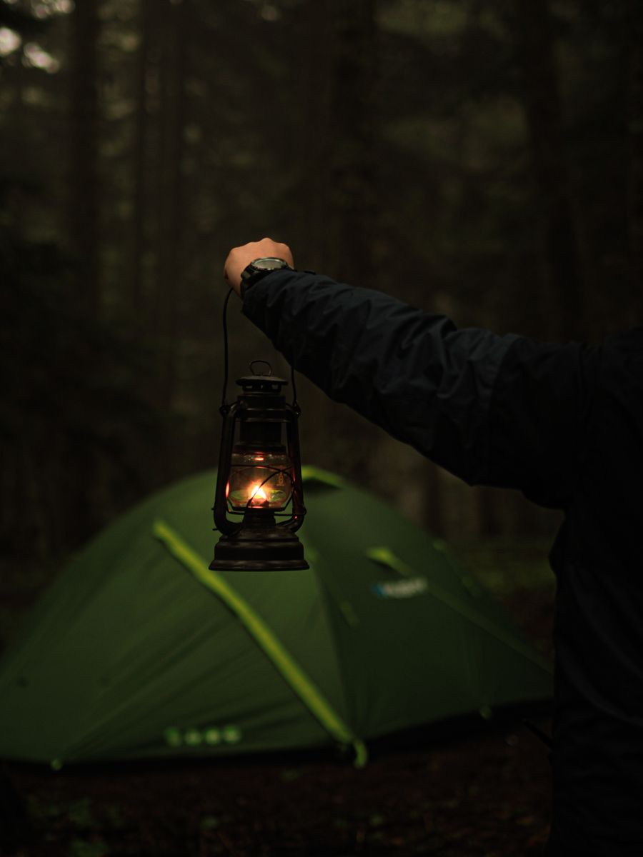 A person holds a lantern near a tent in a dark forest, capturing the essence of nighttime camping. Stock Photo