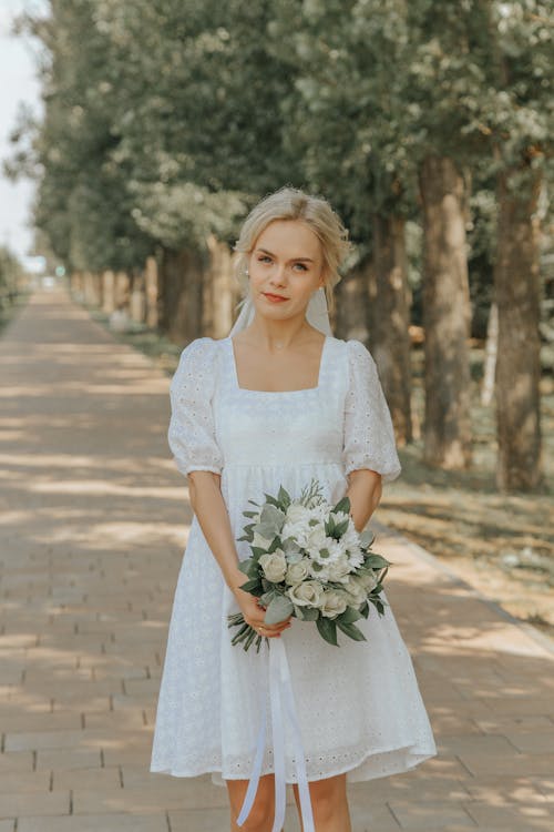 Woman in White Dress Holding Bouquet of Flowers