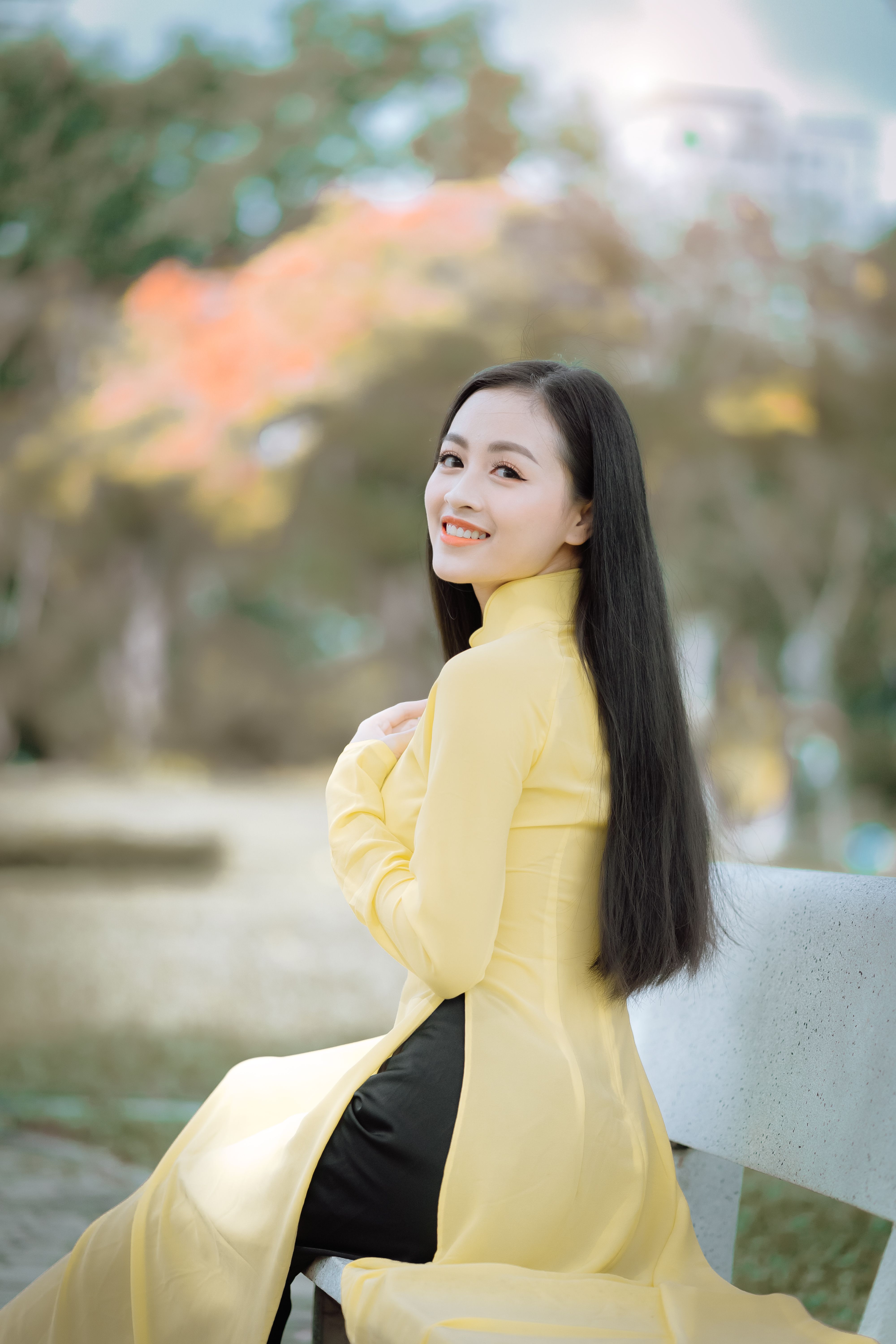 A young woman in a traditional yellow Ao Dai smiling beautifully in a serene outdoor setting.