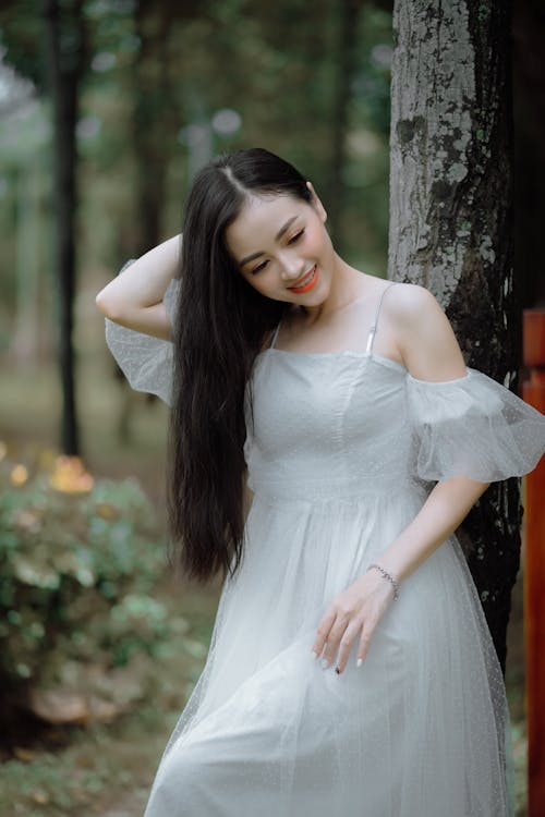 A Woman in Gray Dress Standing Beside Tree Trunk