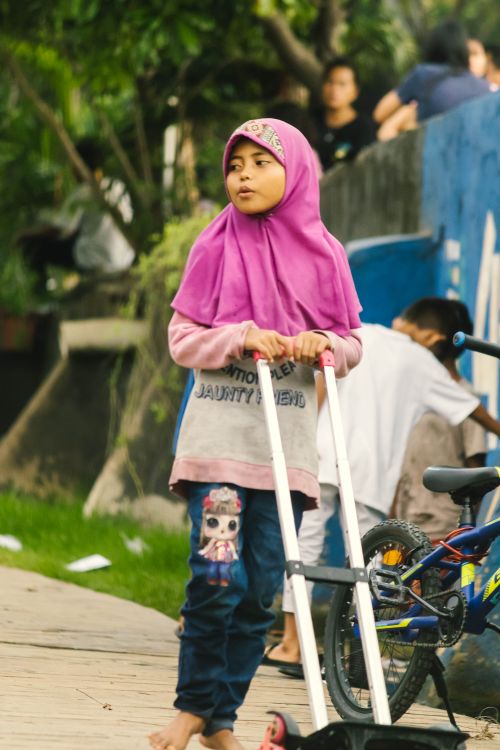 Free A young girl in vibrant attire pushing a cart in a bustling outdoor market setting. Stock Photo