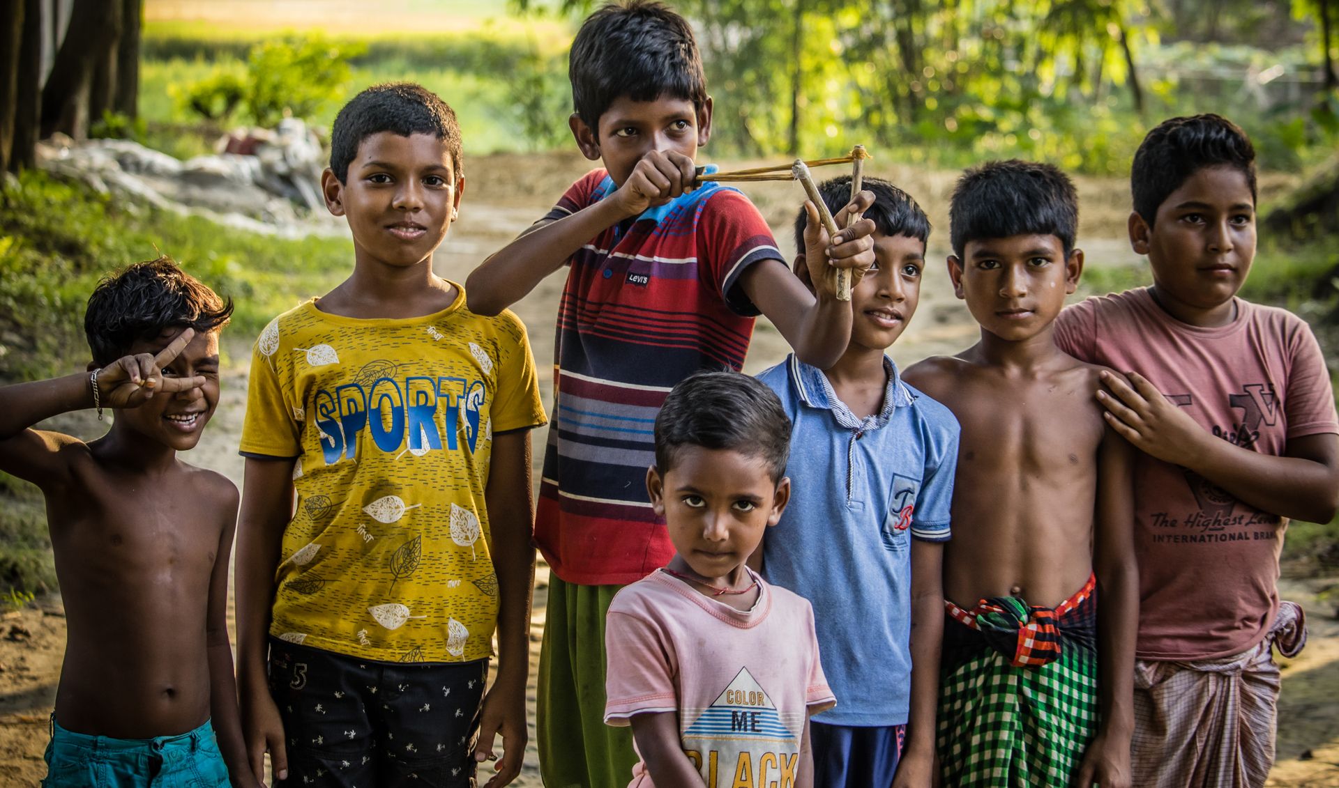 A group of smiling children playing with a slingshot outdoors on a sunny day.