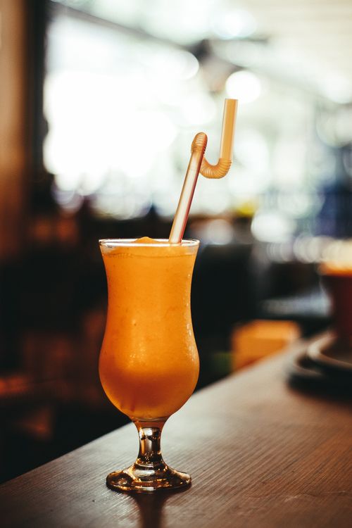 Free Vibrant citrus cocktail in a curvy glass with a straw, perfect for summer vibes. Stock Photo